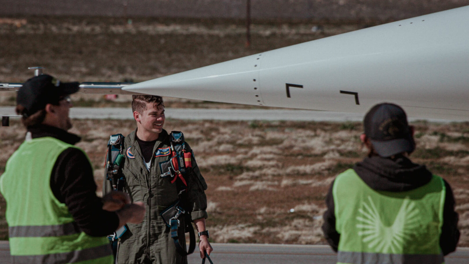 This image shows Tristan 'Geppetto' Brandenburg behind the nose of XB-1 and two Boom employees on the runway at the Mojave Air & Space Port.